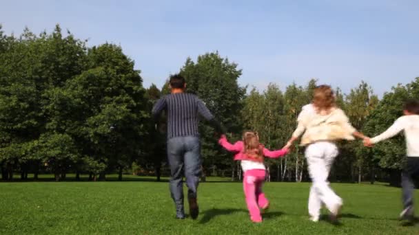 Семья с мальчиком и девочкой держит за руки бежит вперед по парку — стоковое видео