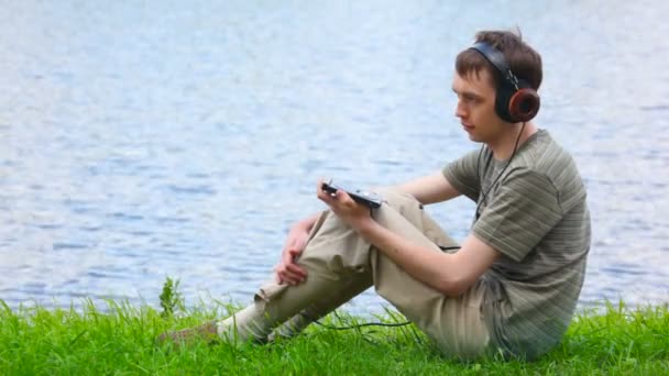 Young man listen music in headphone on water background — Stock Video