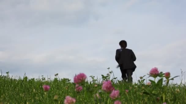 Όμορφος άντρας που τρέχει στο τομέα της πράσινο γρασίδι και λουλούδια πεδίο — Αρχείο Βίντεο