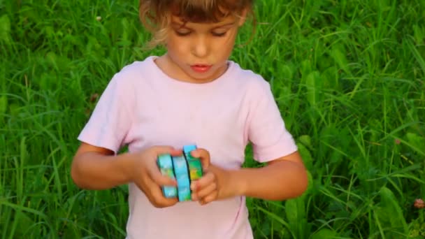 Liten flicka löser Rubiks kub på grönt gräs bakgrund — Stockvideo