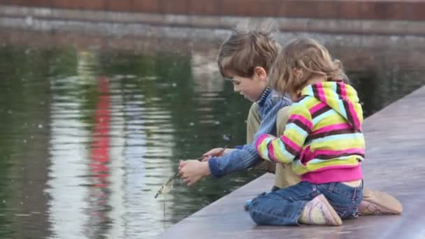 Niño y niña jugando a la pesca en el estanque de la ciudad — Vídeo de stock