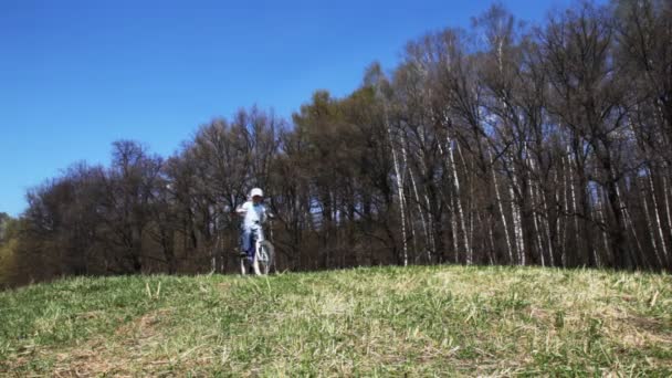 Boy goes on bicycle across the field in spring — Stock Video