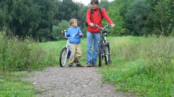 Homem com menino falando, depois andando de bicicleta no parque — Vídeo de Stock