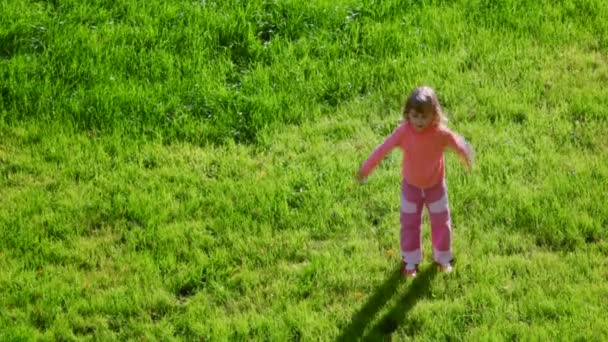 Yeşil çimenlerin üzerinde atlama ve el sallayarak küçük kız — Stok video