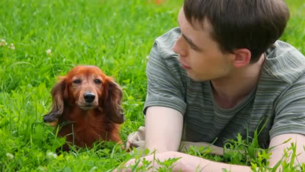 Hombre acostado sobre hierba verde hablando con el perro — Vídeo de stock