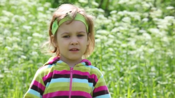 Маленькая девочка в фиолетовой блузке на зеленом поле идет к камере — стоковое видео