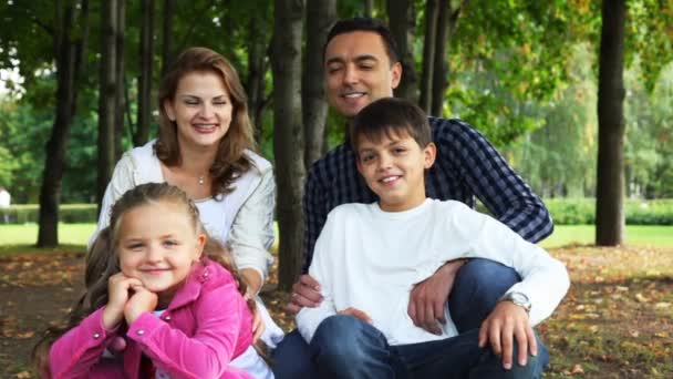 Семья с парнем и девушкой сидит в парке и улыбается — стоковое видео