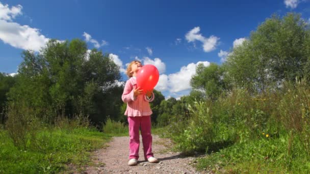 Маленькая девочка играет с красным шаром в парке, шарик лопнул — стоковое видео