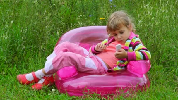 Petite fille avec téléphone couché sur fauteuil gonflable — Video