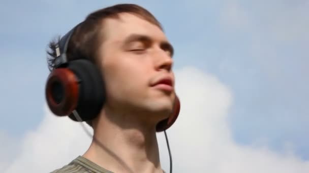 Young man listen music in headphone on sky background — Stock Video