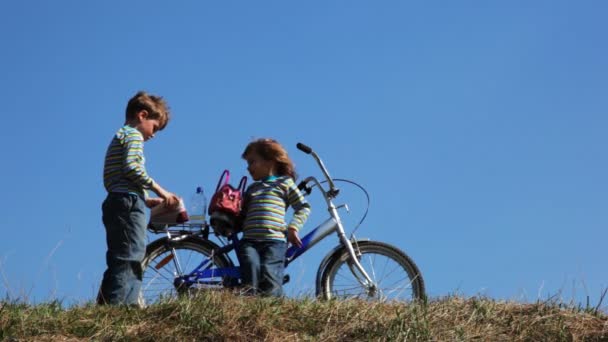 Niño y niña en el campo de estancia cerca de la bicicleta y tomar de las bolsas de juguetes en el campo — Vídeos de Stock