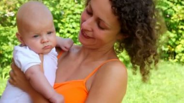 Anne konuşuyor ve onu elinde tutarken bebeğe, gülümseyen