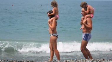 sörf adam ve küçük kızlar omuzları üzerinde yürür plajı ile deniz tutan kadın