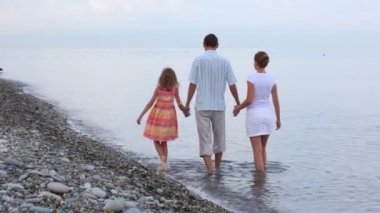 Deniz sörfünde yürüyen üç kişilik aile, el ele tutuşun, kameraya.