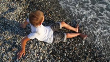 genç çocuk çakıl plajı üzerinde oturur ve denizde, üstten görünüm görünüyor