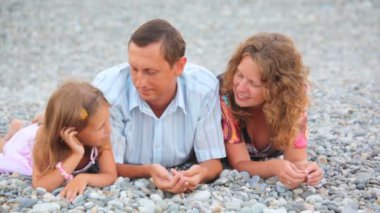 çakıl plajı üzerinde yalan ve konuşurken üç kişinin gülümseyen aile