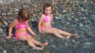 iki küçük kızlar çakıl plajı ile deniz üzerinde oturan gülüyor sörf