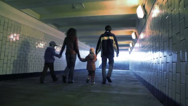 famille de quatre marchant dans le passage souterrain de la caméra, mains jointes 