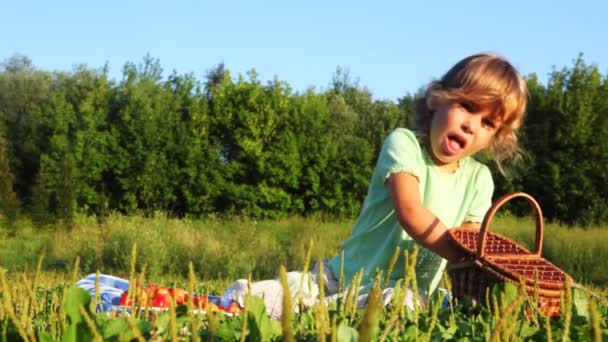 Meisje zit op gazon in gras, eet cherry en spuugt stenen — Stockvideo