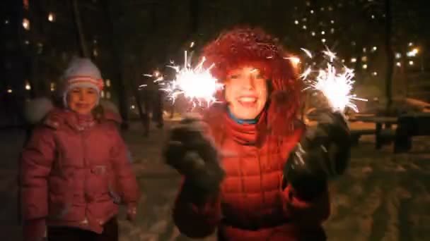 Jovem mulher com sparkler, perto de menina, noite ao ar livre — Vídeo de Stock