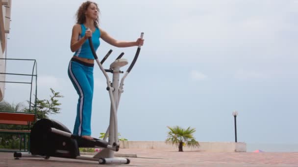 Happy young curly-headed woman on training apparatus outdoor — Stock Video