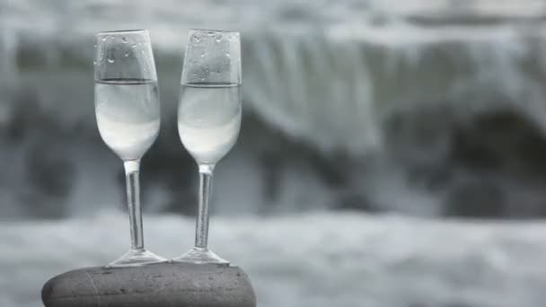 Two glasses with wine standing on stone on beach, sea surf in background — Stock Video