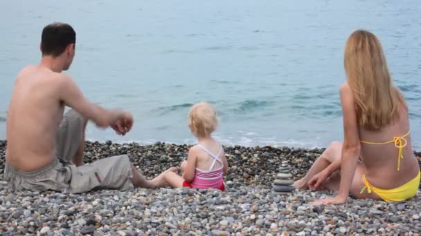 Rodzina siedzący na kamienistej plaży i rzucanie kamieni w morze — Wideo stockowe