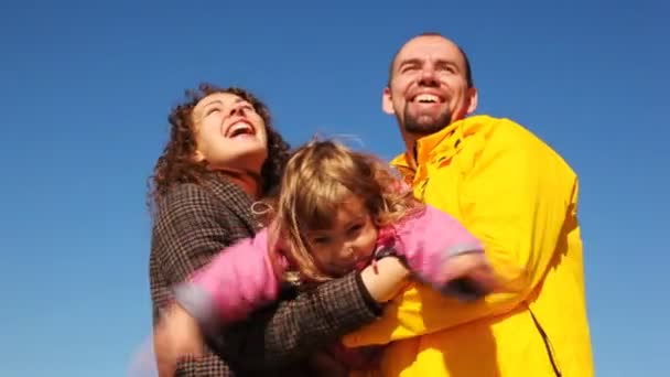 Mum and daddy shakes daughter on hands and all of them smile against clear sky — Stock Video