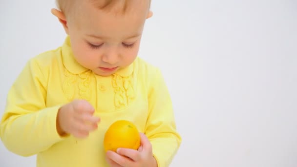 Malá holčička loupání pomeranče proti Bílému pozadí — Stock video