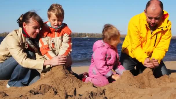 Familj av mon, pappa, son och dotter bygga kullar av sand tillsammans på river beach — Stockvideo