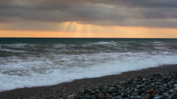 Tenger kavicsos tengerparton napnyugtakor ég, az eső felhők alatt surf — Stock videók