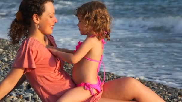 Young mother with her little daughter playing in pebble beach near sea — Stock Video