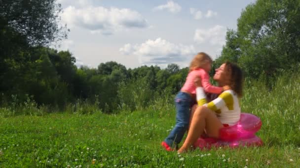 Lilla dotter går till mor sitter på uppblåsbara seat och omfattar — Stockvideo