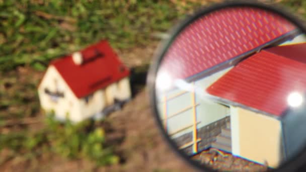 Två leksak hus är tittat igenom av förstoringsglas i park — Stockvideo