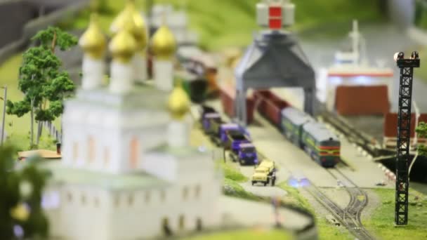 おもちゃの列車は教会の近くの近代的なおもちゃの街の貯蔵所から鉄道上の空の貨物ワゴンをもたらす — ストック動画