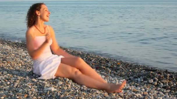 Jeune femme heureuse s'amuse assis ob plage de galets, mer en arrière-plan — Video