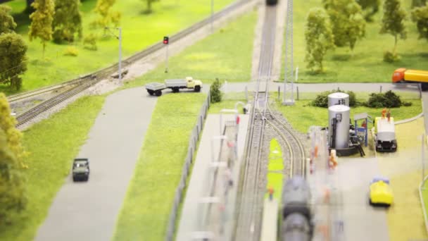 Train pushes tank on rail in modern toy city to fuel station among roads with small cars and trees — Stock Video