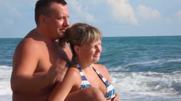 Casal feliz sentado na praia de seixos, mar surf no fundo — Vídeo de Stock