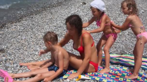 Mujer joven con niños en la playa, extendiendo bronceador unos a otros — Vídeo de stock