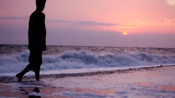 Silhouette dell'uomo che cammina alla macchina fotografica sulla spiaggia, mare del tramonto sullo sfondo — Video Stock