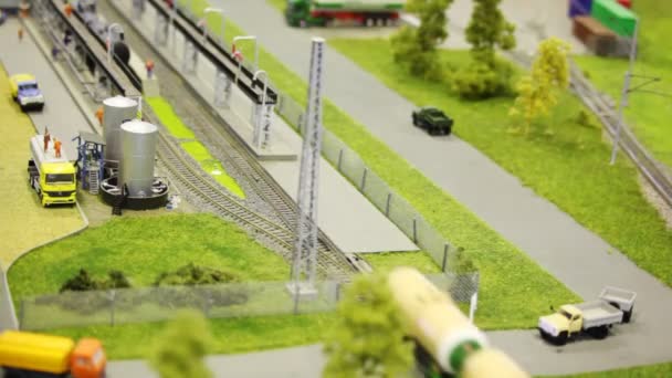 Train pushes tank wagon on rail in modern toy city to fuel station among roads with small cars and trees — Stock Video