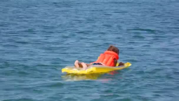 Lächelnder kleiner Junge in Schwimmweste rudert auf aufblasbarer Matratze im Meer — Stockvideo