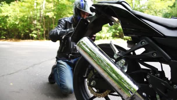 Rowerzysta laczy rejestracyjne na czarny motocykl w parku — Wideo stockowe