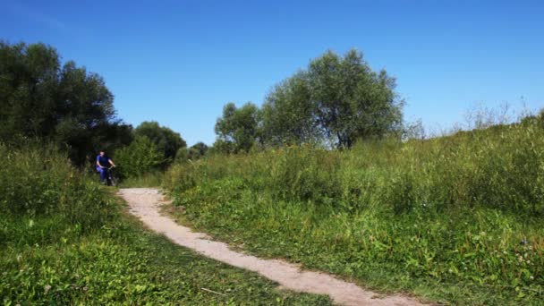 Hombre a su vez traje deportivo azul y niño en chaleco rosa volver uno tras otro en bicicletas en el sendero en el parque — Vídeos de Stock