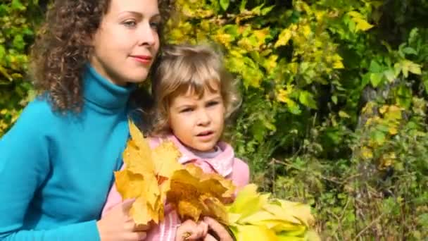 Woung vrouw en klein meisje met bladeren zitten in de herfst park — Stockvideo