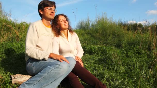 Couple sits close on green herb, talk and smile in park in summer — Stock Video