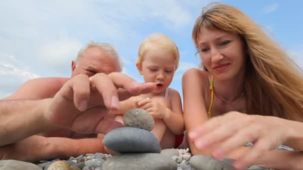 Familia feliz de niña, madre y abuelo mintiendo y hablando en la playa de guijarros — Vídeo de stock
