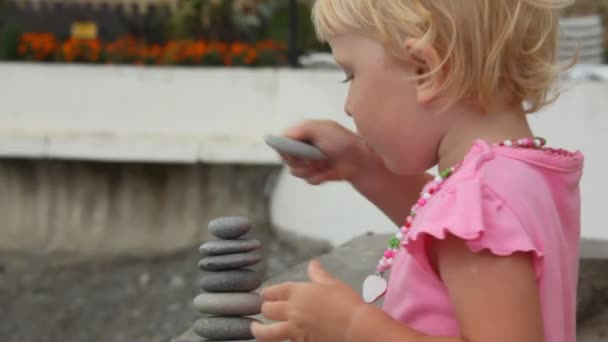 Piccola ragazza bionda costruzione pila di pietre da forno all'aperto — Video Stock