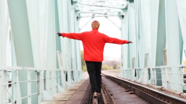 Jeune homme roux marcher en avant sur le rail sur le pont, ayant largement placé les mains — Video