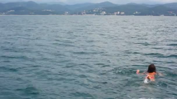 Jeune femme nageant en mer depuis la caméra, côte de montagne en arrière-plan — Video